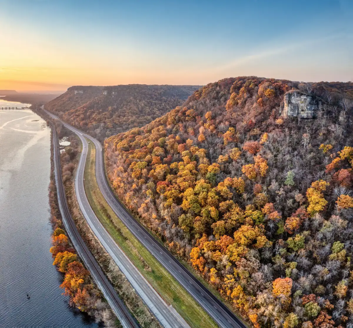 A highway running along the foot of a wooded bluff in autumn near Minneiska, Minnesota