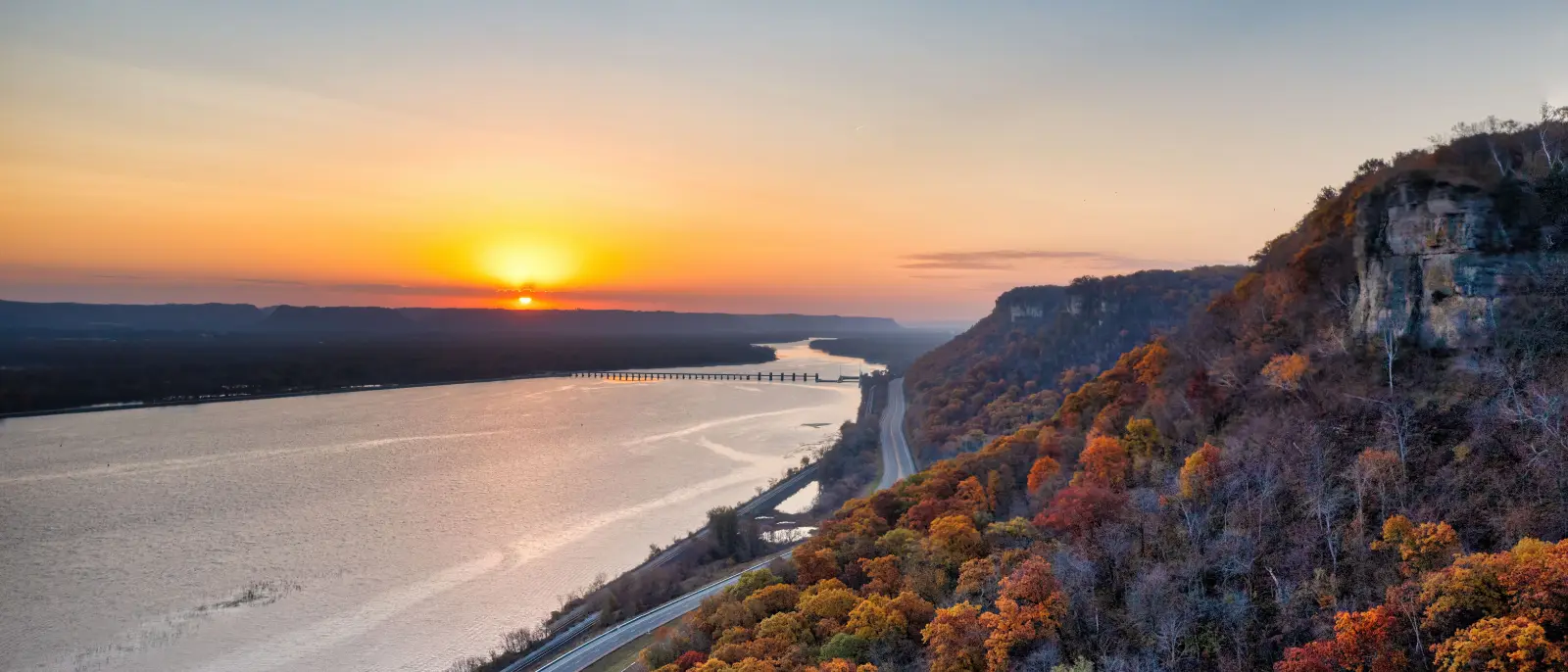 Mississippi River bluffs at sunset, autumn colour running down the wooded slope above the highway corridor