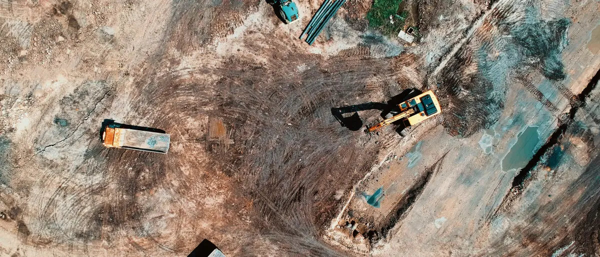 Overhead view of a cleared commercial site, excavator and haul trucks working across churned ground