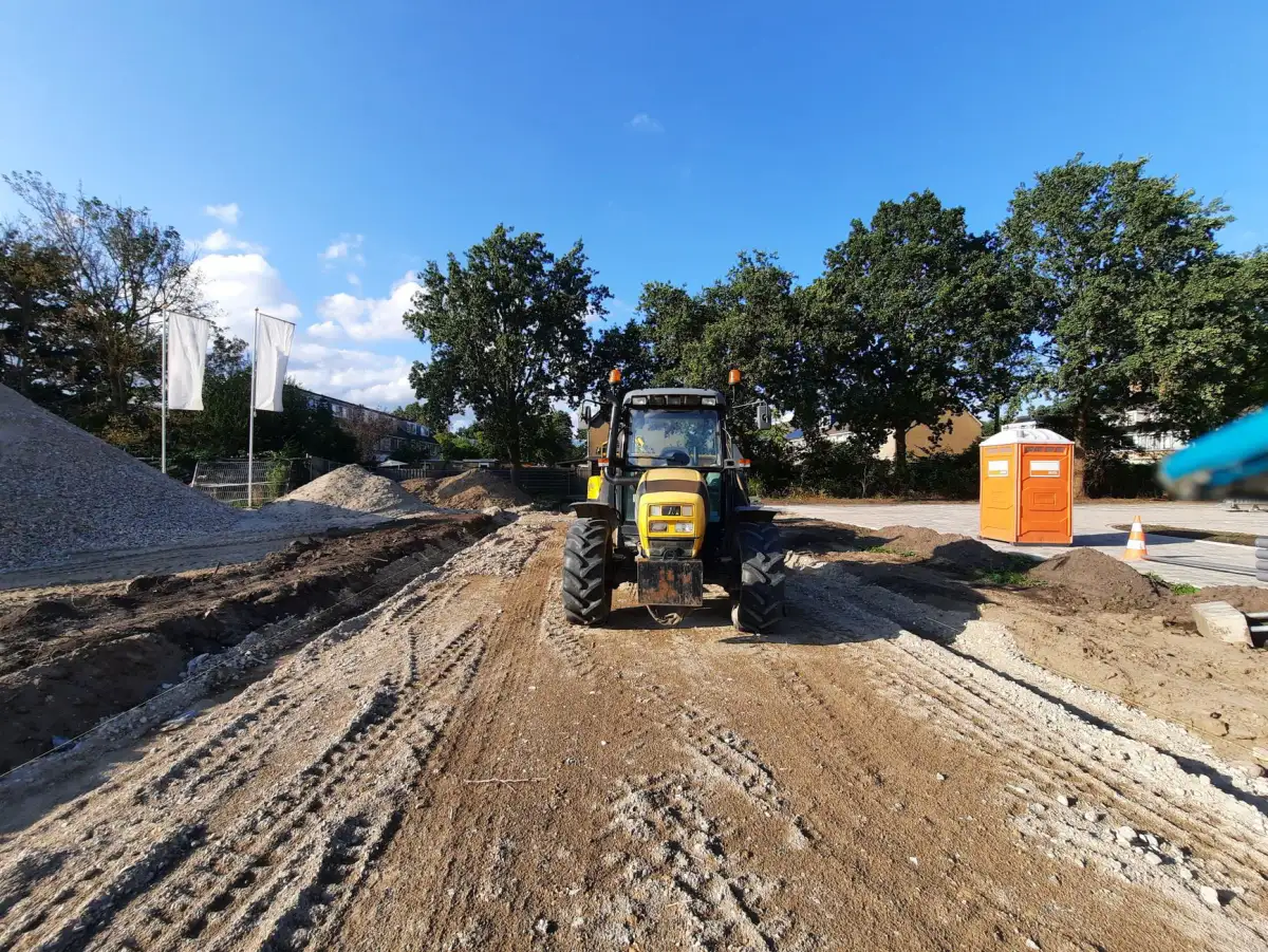 Tractor working a development lot with a dirt access road and standing trees behind