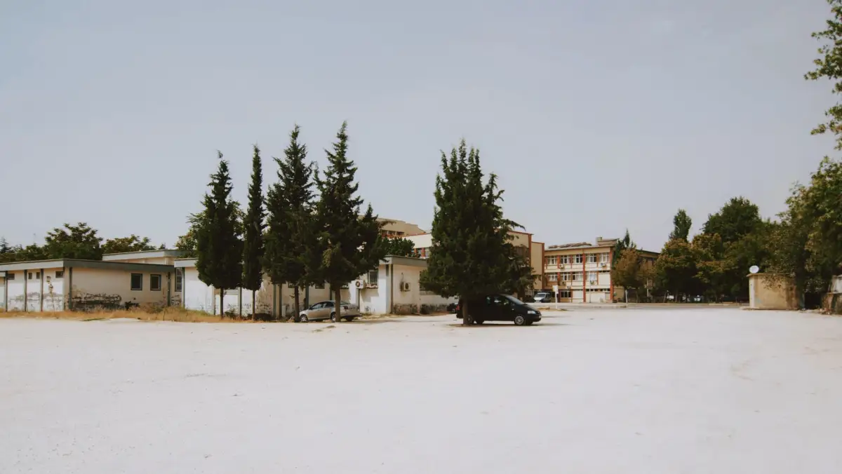 Wide view of a commercial lot with buildings and mature trees under a clear sky