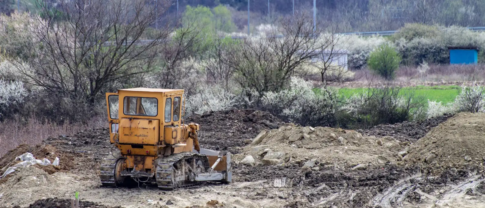 Dozer pushing spoil across a half-cleared lot, brush and scrub still standing along the far tree line